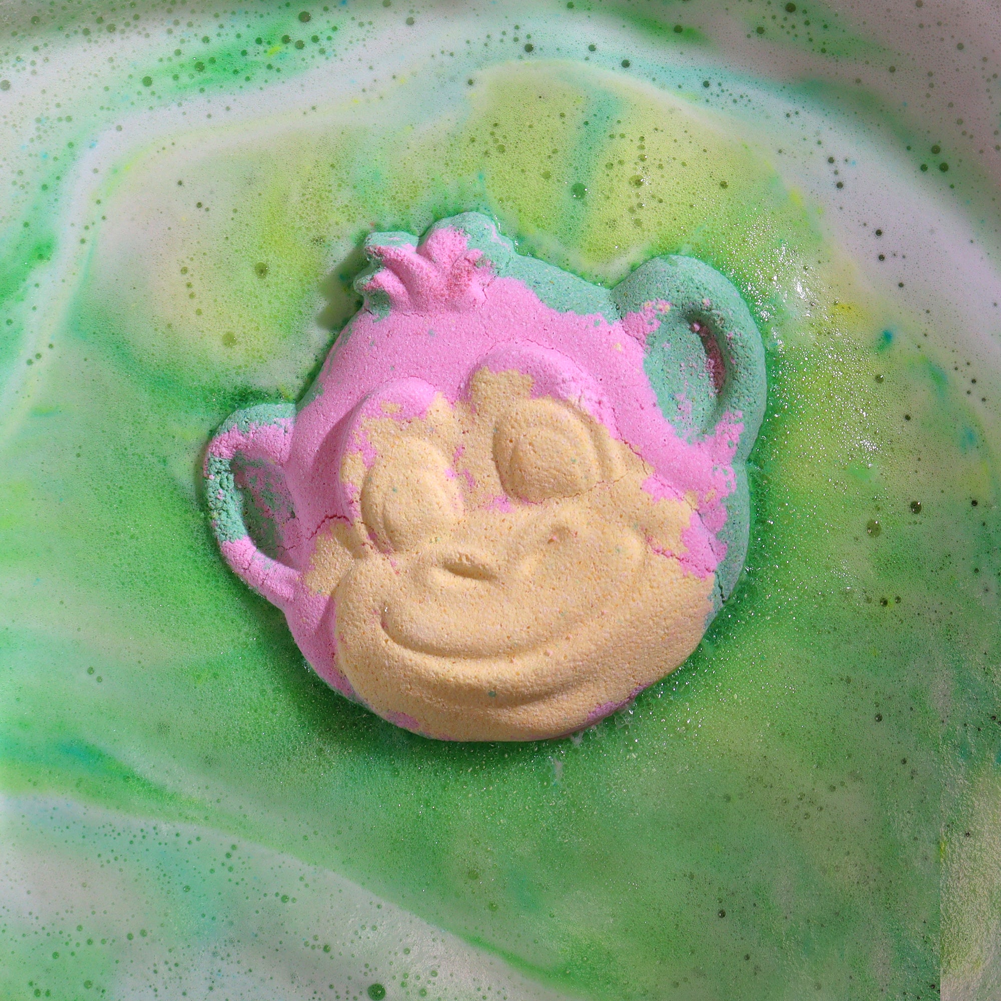 Colorful bath bomb with a frog design on a green and pink liquid surface