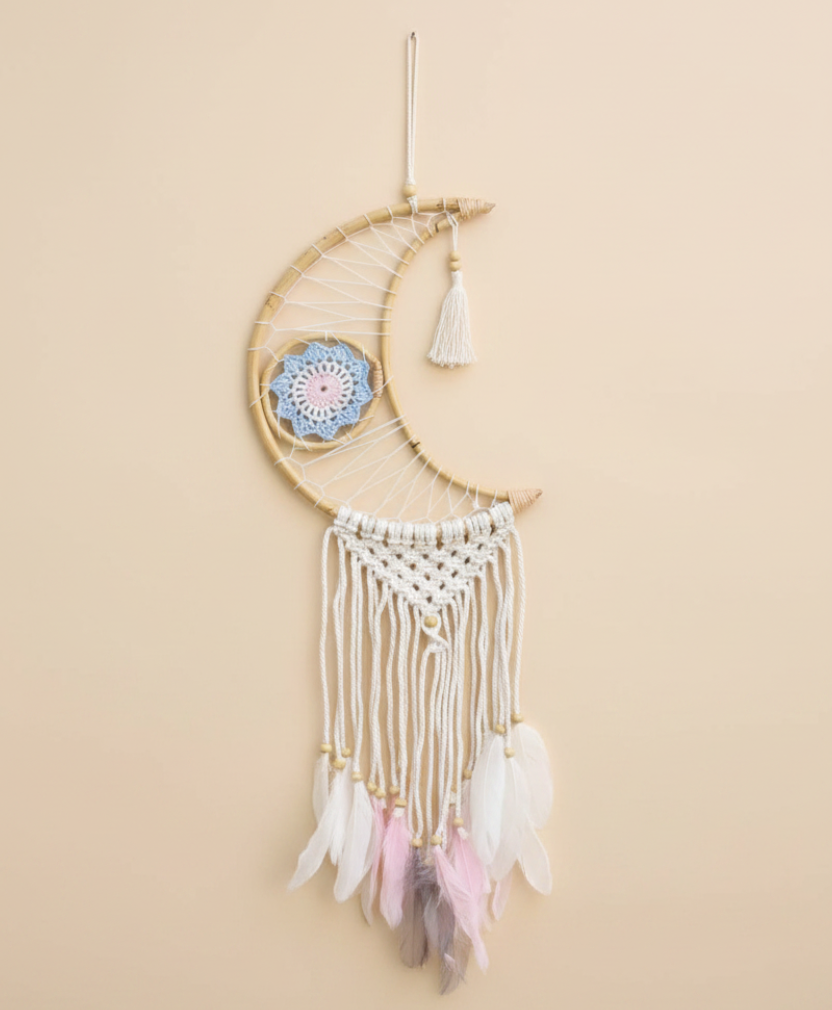 Decorative dreamcatcher with feathers hanging against a beige background