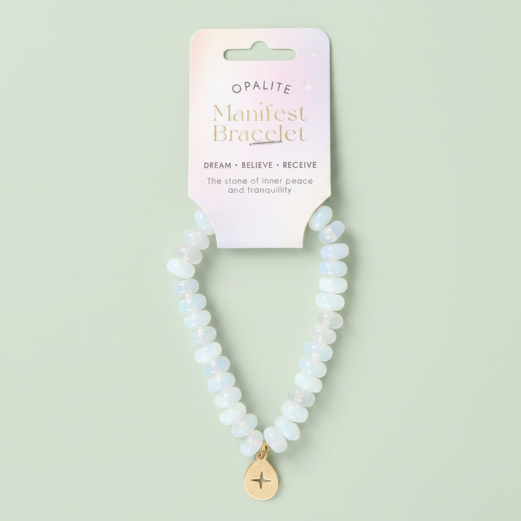 An Opalite Manifest Bracelet featuring light blue and white opalite beads with a gold-toned star charm, displayed on its pastel pink backing card.