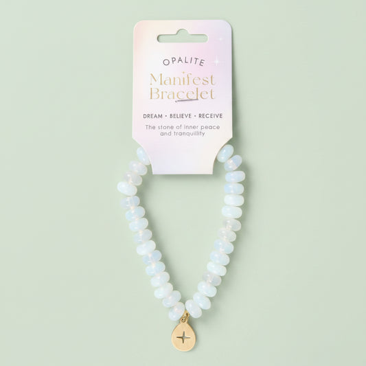 An Opalite Manifest Bracelet featuring light blue and white opalite beads with a gold-toned star charm, displayed on its pastel pink backing card.