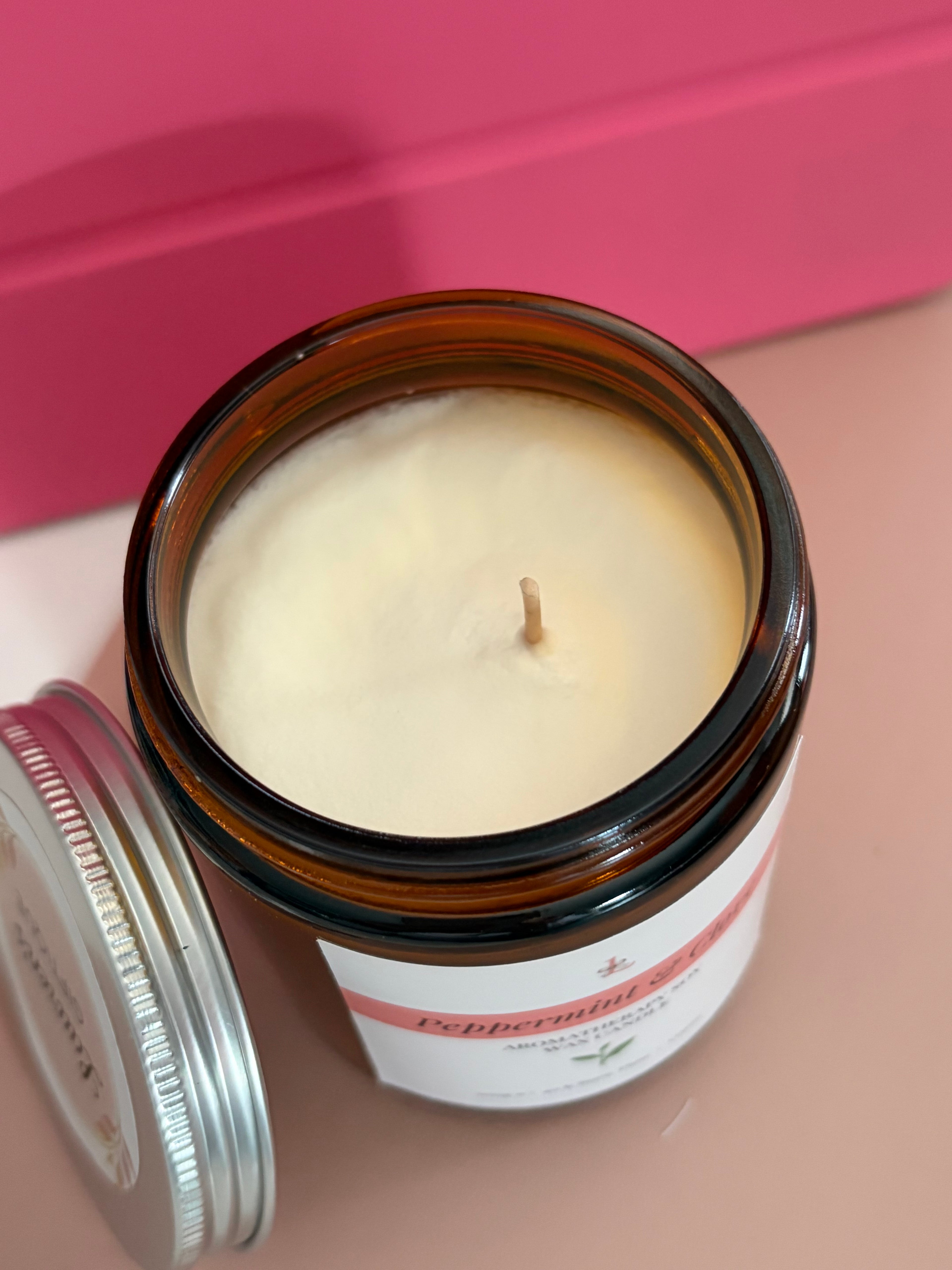 Candle in a glass jar with a visible label on a pink background