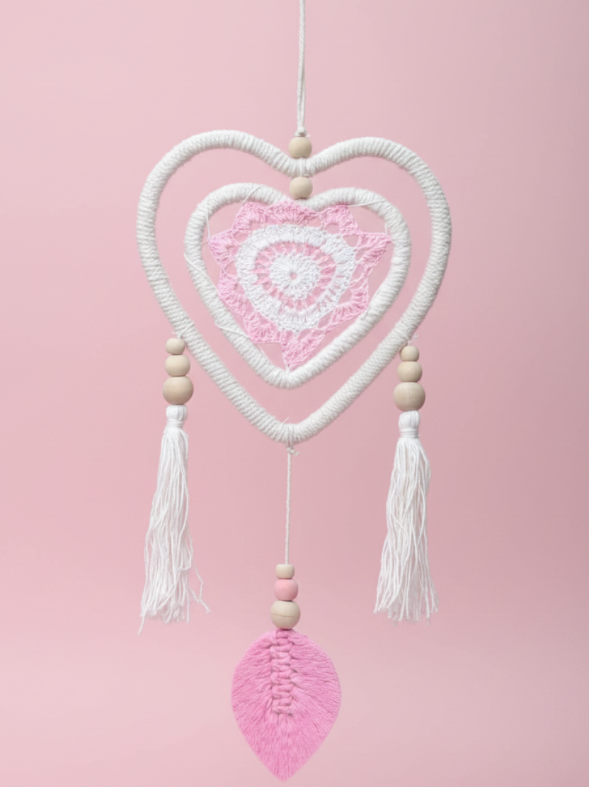 Heart-shaped crocheted dreamcatcher with tassels and beads against a pink background