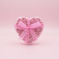 Heart-shaped arrangement of pink roses with a polka dot ribbon on a pink background