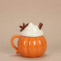 Pumpkin-shaped mug with a lid resembling whipped cream and chocolate leaves on a brown background