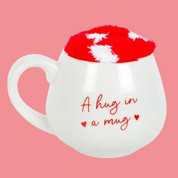 White mug with red interior, red heart-shaped pillow, and text 'A hug in a mug' on a light background