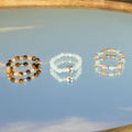 Three gemstone rings on a reflective surface with a blurred natural background