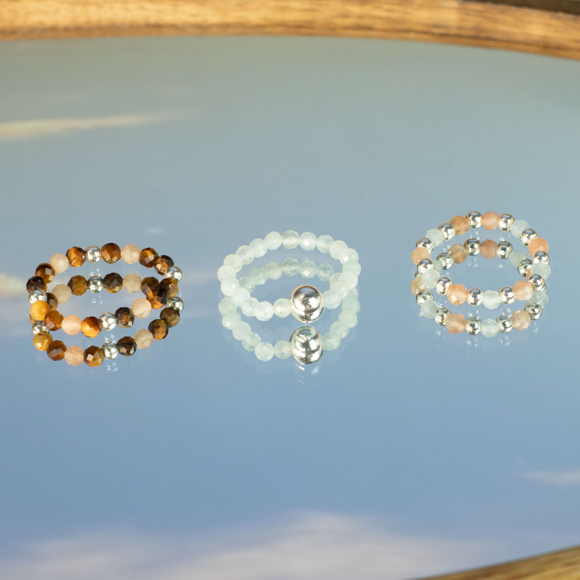 Three gemstone rings on a reflective surface with a blurred natural background