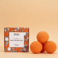 Orange bath bombs with packaging labeled 'Ancient Wisdom Vitamin C Bath Bombs Set' on a orange background